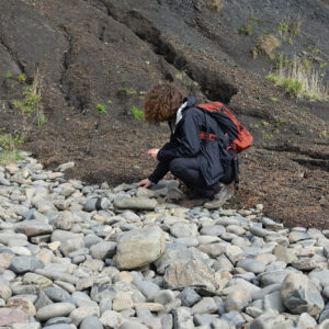 a person crouched on the ground looking through rocks